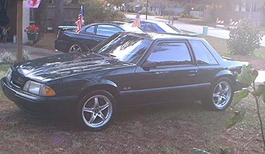 Dark green coupe with "5.0" badge and aftermarket wheels parked on grass.