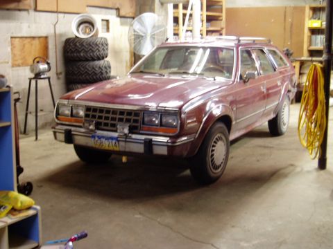 2000 Ford E350 - A maroon station wagon is parked in a garage. The vehicle is viewed from a front three-quarter angle, showing its grille, headlights, and f…