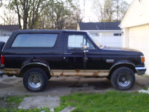 Side view of a black Ford Bronco with rust on the lower body panels.