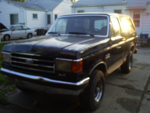 Black 1990 Ford Bronco parked in a driveway at sunset.