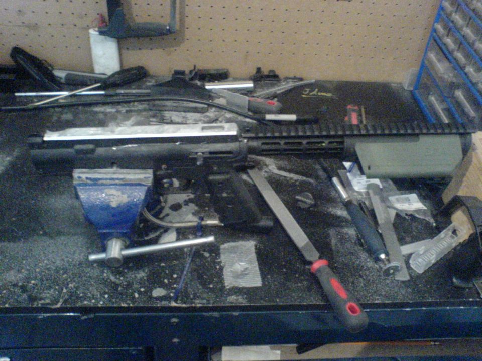 Workbench with tools and firearm parts, including a vise and files.