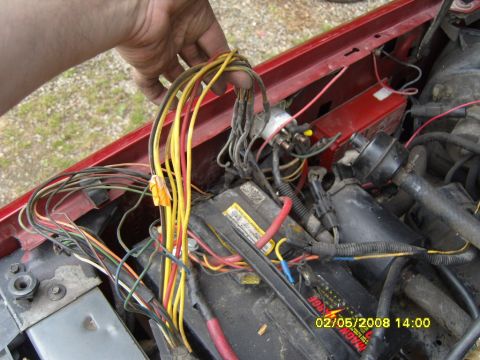 1989 Ford Bronco - A close-up view of a tangled bundle of colorful wires being held by a hand over a car battery and engine components. The vehicle appears to…