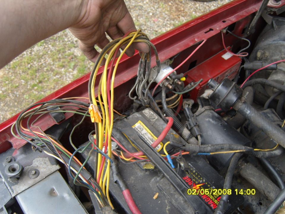 Close-up of a hand holding a bundle of wires over a car battery and engine components in a red vehicle.