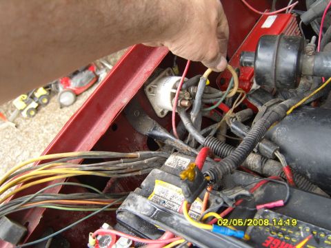 1989 Ford Bronco - A person's hand is shown working on the electrical wiring of a red vehicle, likely under the hood. The focus is on the complex network of w…