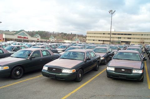 2001 Ford Crown Victoria - Dozens of green-over-tan two-tone Ford Crown Victoria fleet sedans packed nose-out across a shopping-center parking lot, most on plain blac…