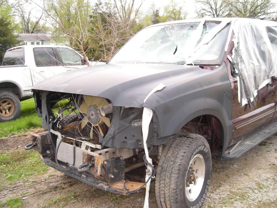 Wrecked maroon Ford Excursion with shattered windshield, taped windows, primered hood, and exposed engine fan.