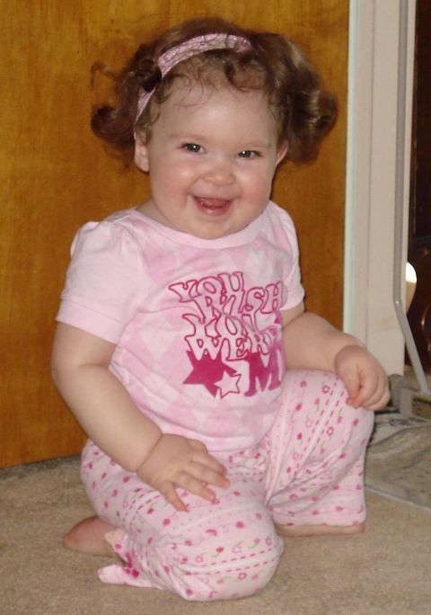 2000 Ford Crown Victoria - A baby girl wearing a pink shirt and pants with a floral headband smiles at the camera while kneeling on a carpeted floor.