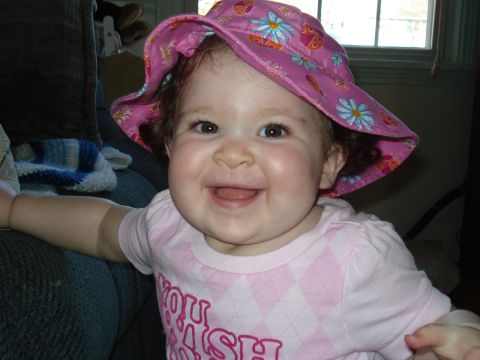 2000 Ford Crown Victoria - A close-up photo of a baby girl wearing a pink sun hat with a floral pattern and a pink shirt with a diamond pattern and text. She is smili…