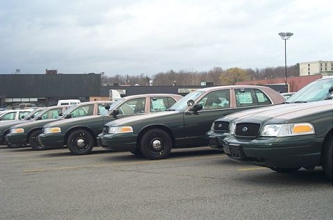 2001 Ford Crown Victoria - Several Ford Crown Victoria sedans are lined up in a parking lot under an overcast sky.