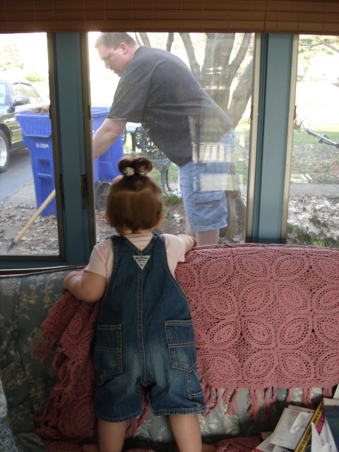 2000 Ford Crown Victoria - A young child wearing denim overalls stands on a couch looking out a window at a man raking leaves near a blue trash can.