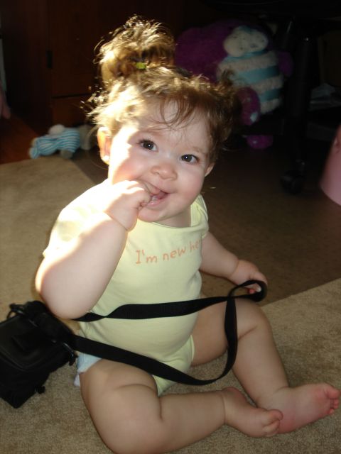 2000 Ford Crown Victoria - A baby girl with her hand in her mouth sits on a carpeted floor, wearing a yellow onesie with the text "I'm new her" visible. A black strap…