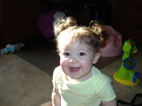 2000 Ford Crown Victoria - A baby girl with blonde curly hair pulled into pigtails smiles at the camera. She is wearing a yellow onesie and sitting on a carpeted floo…