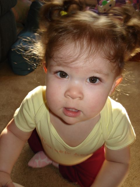 2000 Ford Crown Victoria - A close-up, high-angle shot of a baby with reddish-brown hair styled in two pigtails. The baby is wearing a yellow onesie with red pants an…