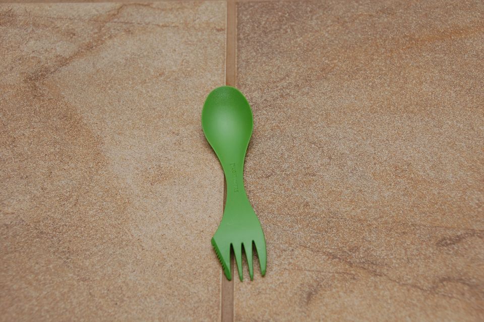 Green plastic spork on a tan tile floor