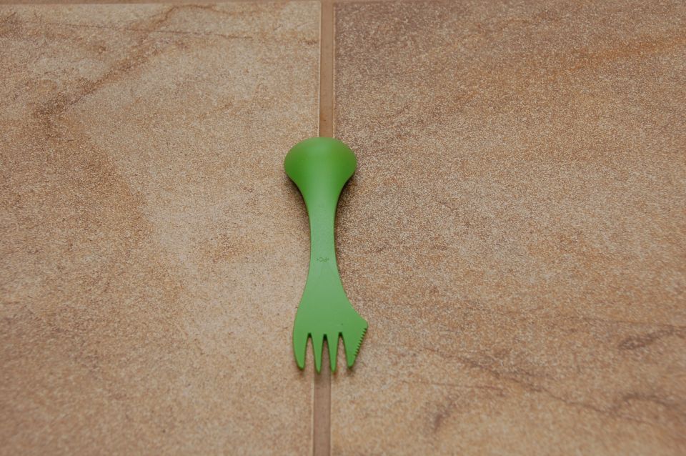 Green plastic spork on beige tile floor