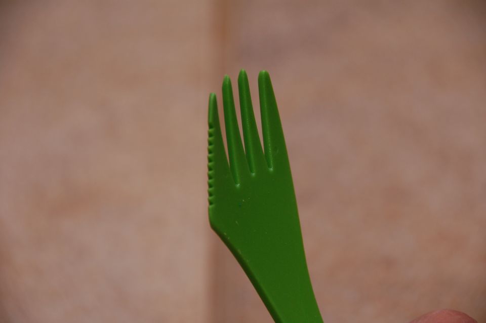Green plastic fork held against a blurred tan background