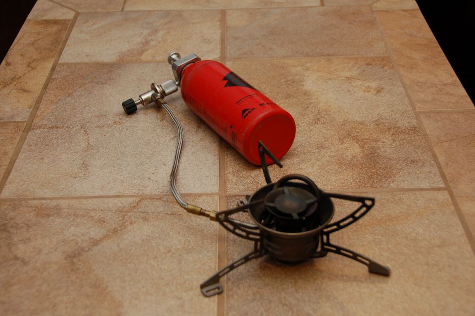 MSR camping stove with red fuel bottle and burner on tile floor