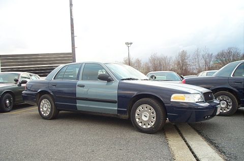 2001 Ford Crown Victoria - A two-tone Ford Crown Victoria is parked in a lot with other vehicles, showing a mix of blue and light blue body panels.