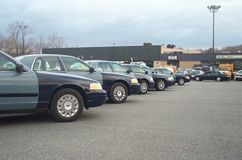 2001 Ford Crown Victoria - Several Ford Crown Victoria police cars are parked in a lot, with a building in the background.