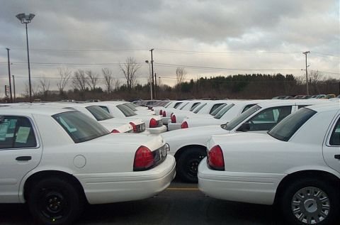 2001 Ford Crown Victoria - Multiple white 2001 Ford Crown Victoria sedans are parked in an outdoor lot under a cloudy sky.