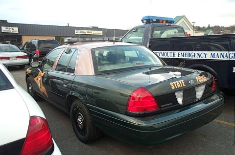 2001 Ford Crown Victoria - A dark green 2001 Ford Crown Victoria police car is parked next to a black truck, with "STATE POLICE" visible on the trunk.