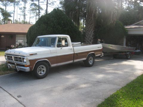 1972 Ford F-100 - A two-tone white and brown 1970s era Ford F-series pickup truck is parked on a concrete driveway. The truck is towing a small aluminum boat…