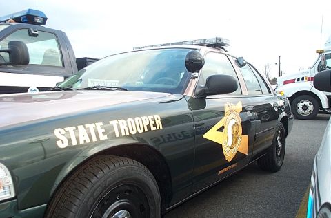 2001 Ford Crown Victoria - A 2001 Ford Crown Victoria police car, marked as "STATE TROOPER", is seen from a 3/4 front angle with other vehicles in the background.