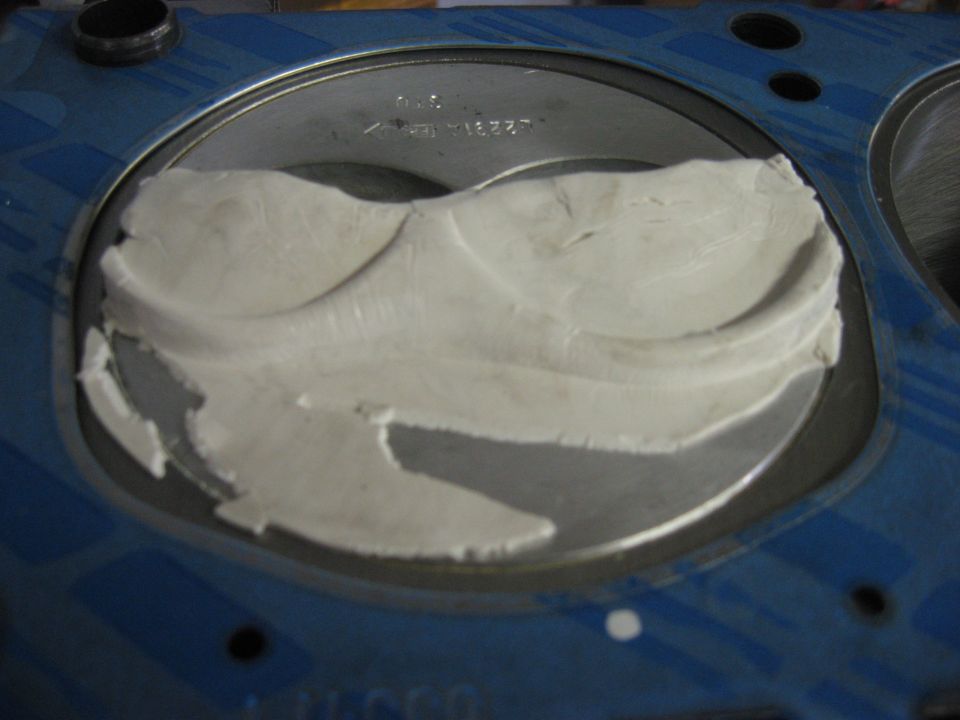 Cylinder head combustion chamber filled with white clay under a blue head gasket opening