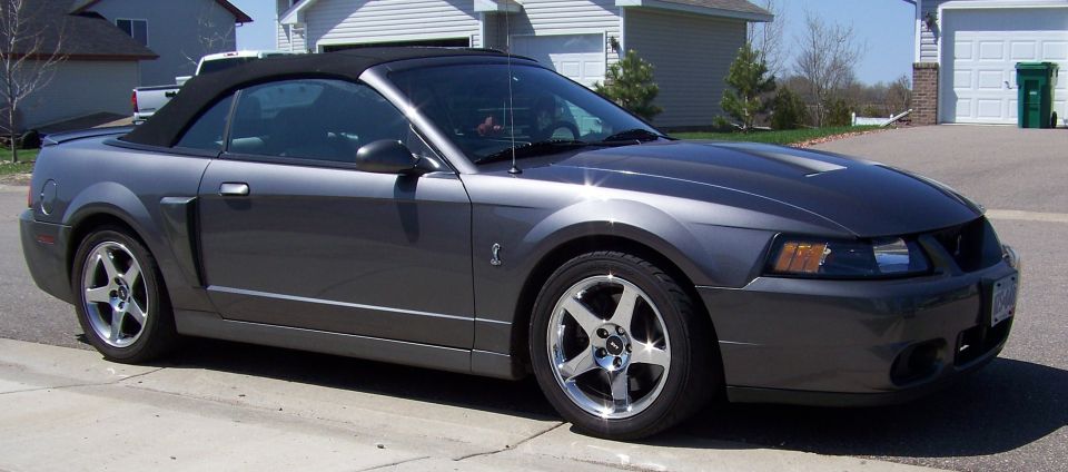Dark gray Ford Mustang convertible parked on a street, side view.