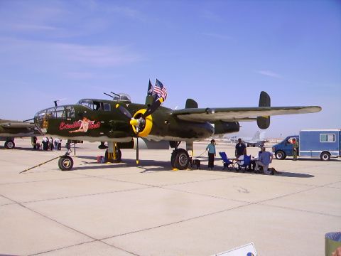 1990 Ford Bronco - A vintage B-25 Mitchell bomber aircraft, painted olive drab with nose art, is parked on an airfield with a group of people gathered nearby.…