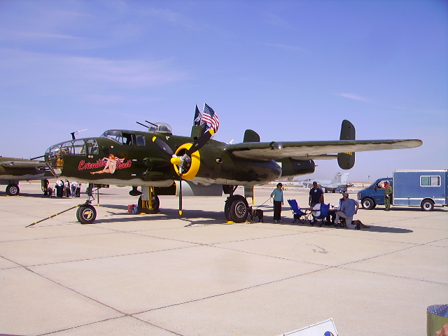 Olive drab B-25 Mitchell bomber with nose art and American flag on airfield.