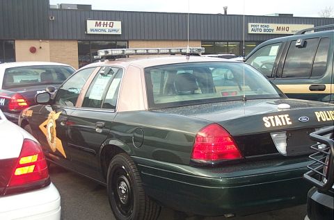 2001 Ford Crown Victoria - A dark green police car with a tan roof and "STATE POLICE" text on the trunk is parked next to other vehicles.
