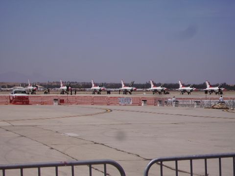 1990 Ford Bronco - A line of fighter jets with red and white markings are parked on an airfield. A white Ford Bronco is parked in front of the first jet.