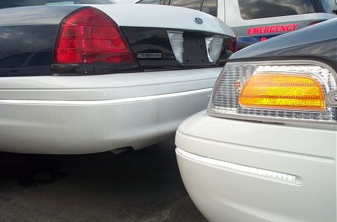 2001 Ford Crown Victoria - Tight shot of two white Ford Crown Victoria sedans, including a marked EMERGENCY unit, parked bumper to bumper.