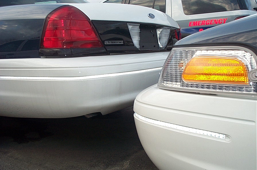 Close-up of two Ford Crown Victoria police cars, rear taillight and front corner lamp, one marked EMERGENCY