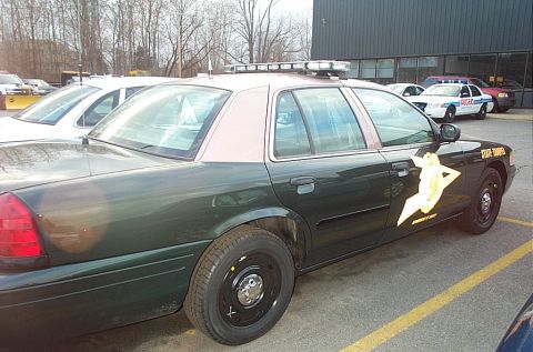 2001 Ford Crown Victoria - A dark green 2001 Ford Crown Victoria police car, likely a state trooper vehicle, is parked next to other cars.