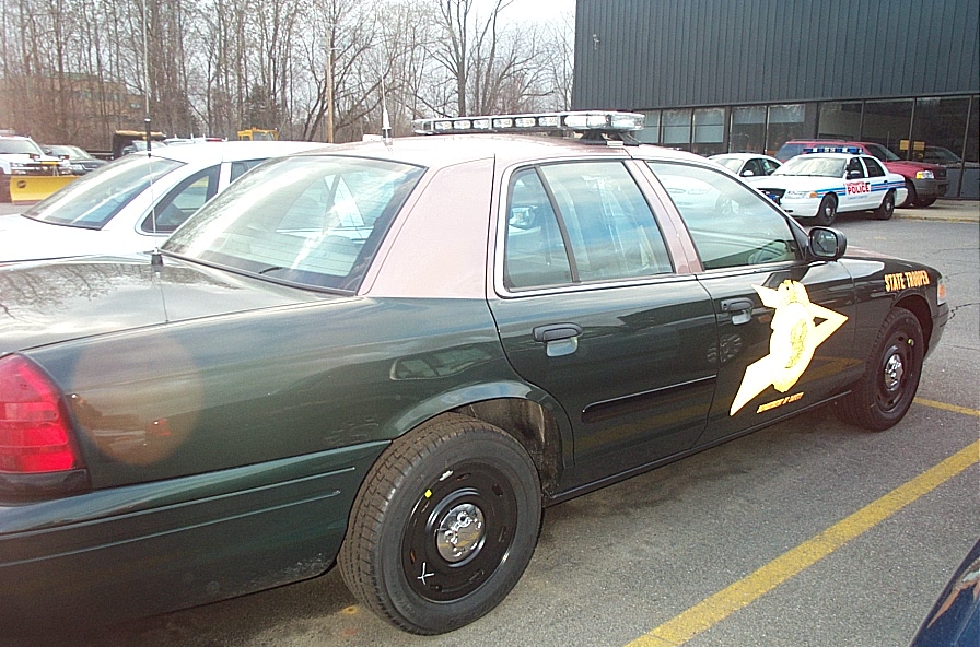 Side view of a dark green 2001 Ford Crown Victoria police car with a state trooper emblem