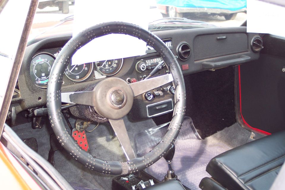 Vintage car interior with black steering wheel, dashboard gauges, and manual shifter.