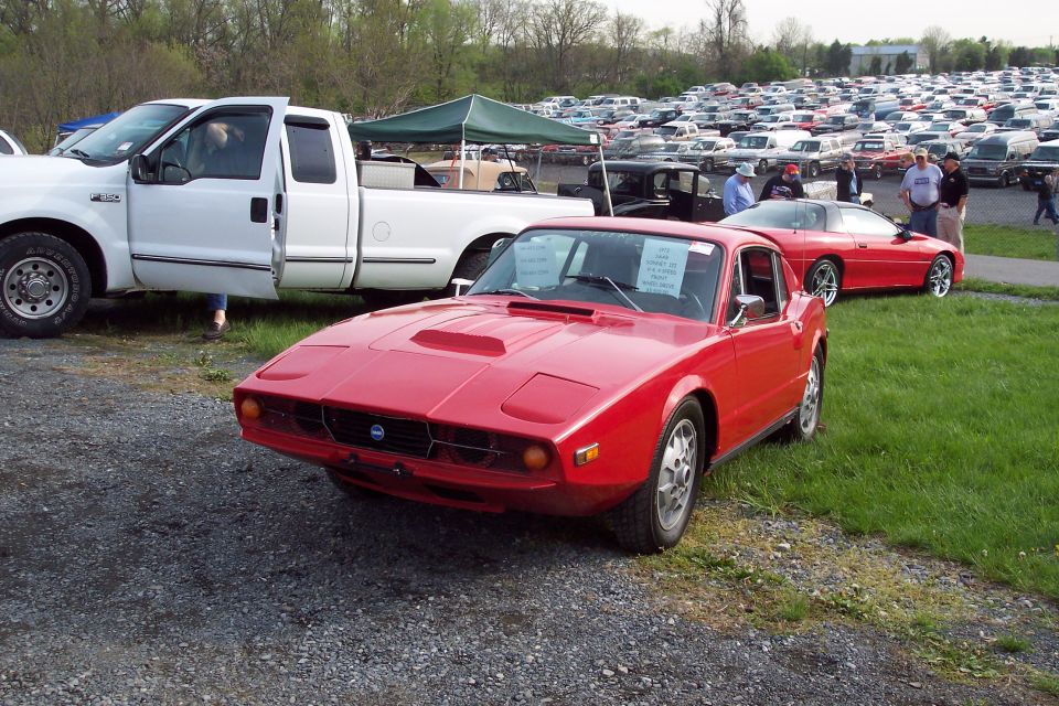Red 1972 Saab Sonett III parked in front of a white Ford pickup truck with many cars in the background.