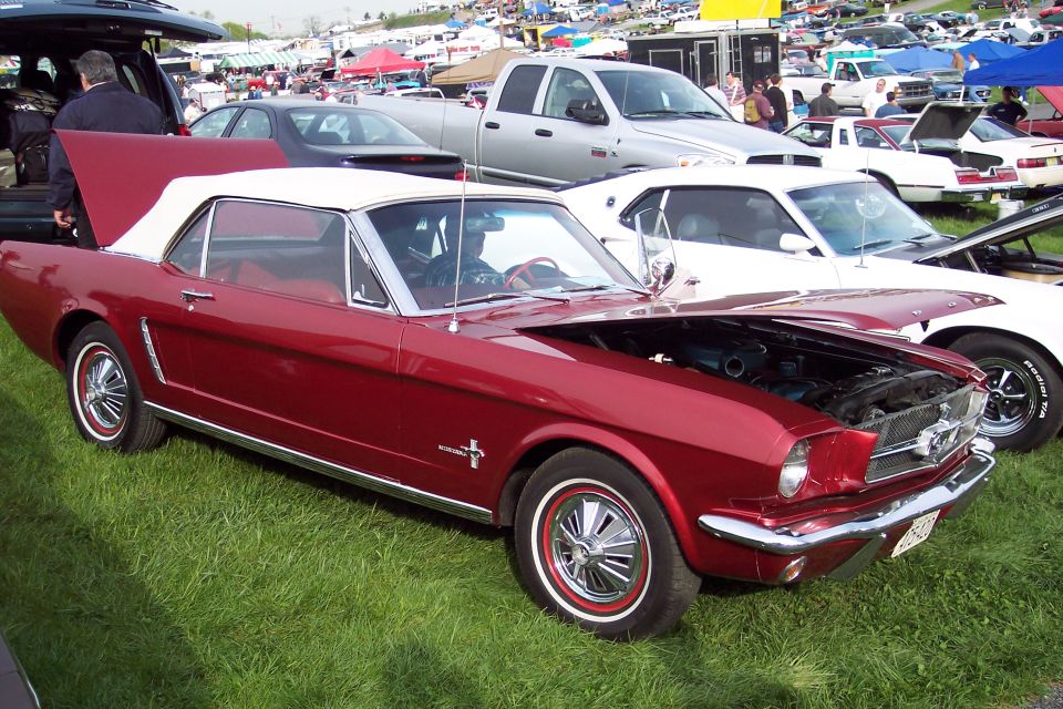 Red 1965 Ford Mustang convertible with hood open, parked on grass.