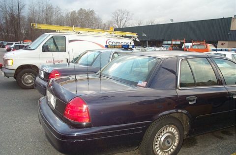2001 Ford Crown Victoria - A dark sedan is parked next to a white van with a ladder rack on top.