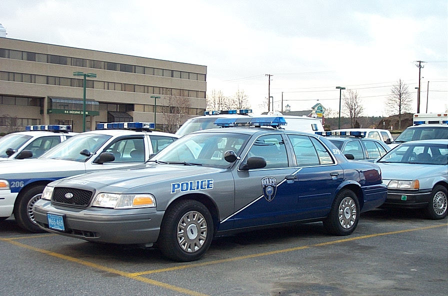 Silver and blue Ford Crown Victoria police cruiser with blue light bar in parking lot