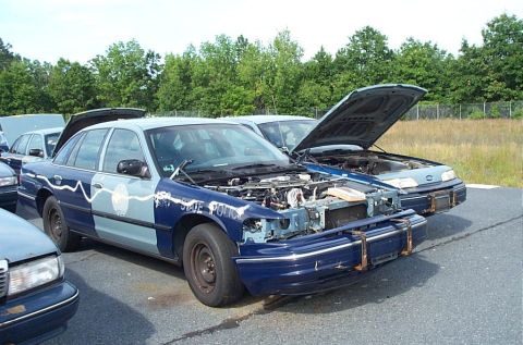 2001 Ford Crown Victoria - This police car, marked 'STATE POLICE', is shown with its hood open, revealing its engine compartment. Another vehicle is visible behind it.