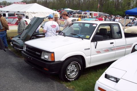 2001 Ford Crown Victoria - A white Mazda B-Series pickup truck is displayed at an outdoor car show with other vehicles and tents in the background.