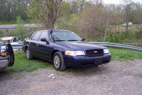 2001 Ford Crown Victoria - A dark blue 2001 Ford Crown Victoria sedan is parked outdoors on a gravel lot.