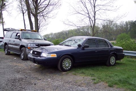 2001 Ford Crown Victoria - A dark blue 2001 Ford Crown Victoria sedan is parked on the side of the road next to a dark SUV.