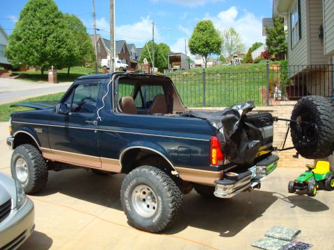 1995 Ford Bronco - A lifted Ford Bronco with its soft top removed sits in a driveway next to a house.