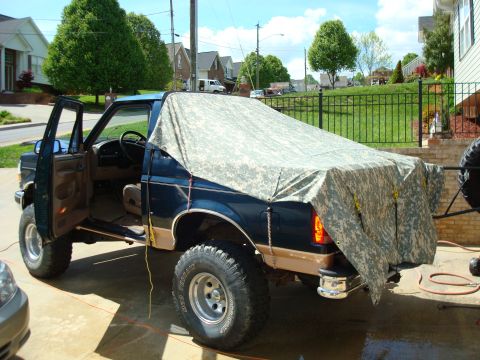 1995 Ford Bronco - A Ford Bronco is parked in a driveway with its doors open and a camouflage tarp over the bed.