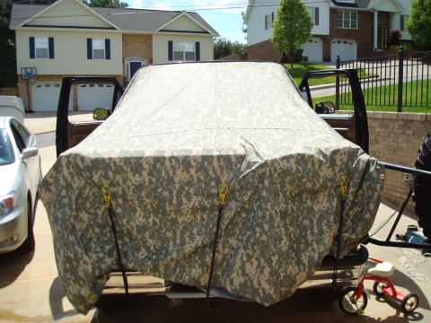 1995 Ford Bronco - A vehicle is covered by a camouflage tarp in a driveway, with its doors open.