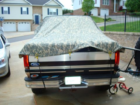 1995 Ford Bronco - A Ford pickup truck is covered with a camouflage tarp, with tools visible on the rear bumper.